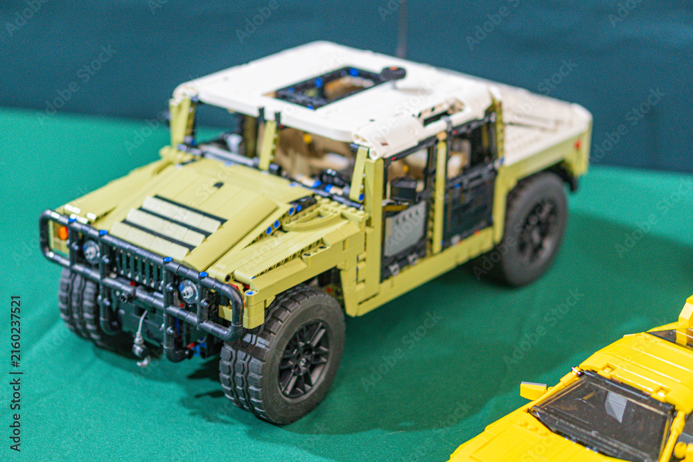 Fototapeta premium Large, robust tan and black Lego jeep with visible interior, flanked by smaller yellow cars on a green surface Bright lighting accentuates colors and textures - Kyiv, Ukraine - June 7, 2025