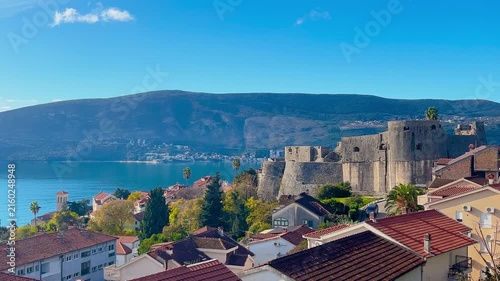Panoramic view of Herceg Novi showing historic fortress, red roof houses and Adriatic Sea with mountains in the background, coastal cityscape and travel destination concept