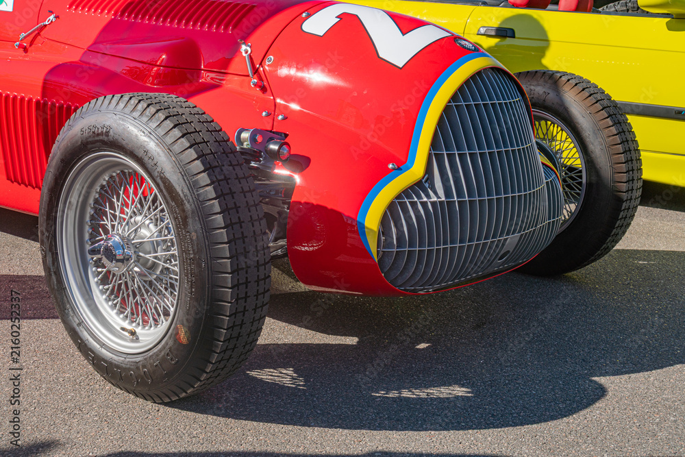 Fototapeta premium Vintage Alfa Romeo Formula 1 car on tarmac racetrack, red with white and yellow accents, round headlights, wire-mesh grille, large spoked wheels, daylight, - Kyiv, Ukraine - September 21, 2025
