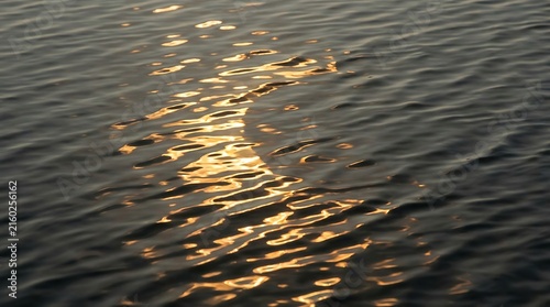 Golden sunset reflection on dark rippling water surface at twilight