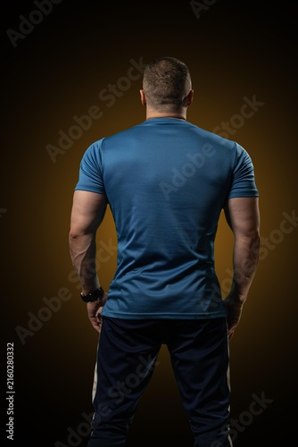 Obraz na płótnie Muscular male athlete stands with his back to the camera inside a dark fitness studio