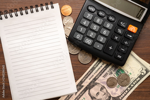 US dollar bills and coins with calculator and blank notebook on a wooden desk, illustrating accounting, cash management, budgeting and everyday expenses.