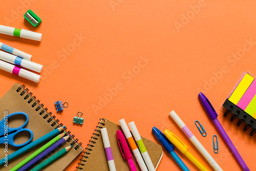 Bright stationery items surround notebooks on a vibrant orange surface, creating an energetic workspace for studying, drawing, planning, and creativity. Copy space.