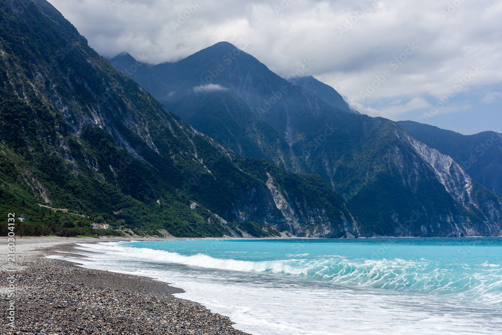 Fototapeta premium Scenic Qingshui Cliff in Hualien, Taiwan. High coastal mountains meet the turquoise Pacific Ocean. Pebble beach with breaking waves under overcast sky.