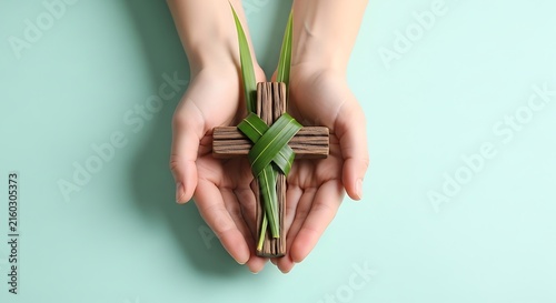 hands gently holding a small wooden cross wrapped with palm leaves
