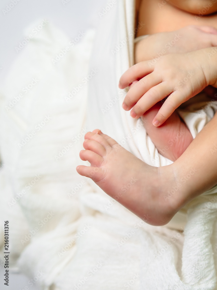 Obraz premium A charming close-up of a newborn's tiny foot stretching out beside delicate folded hands, wrapped in textured white blankets for a cozy studio shot.