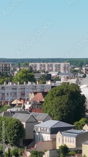 Nevers, France, showing a mix of modern apartment blocks and traditional French houses surrounded by lush green trees under a clear blue sky, aerial vertical 9:16 view.