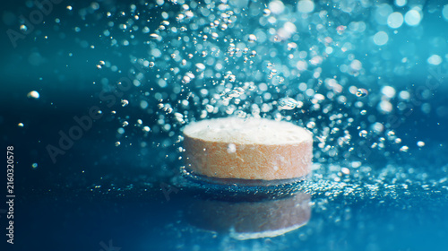Macro photography of an orange effervescent tablet dissolving in water, producing a beautiful vibrant splash with numerous oxygen bubbles rising, perfect for pharmacy advertising.
