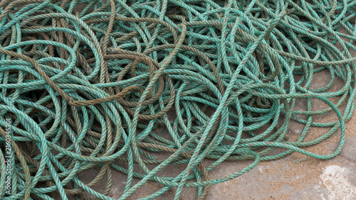 Coiled turquoise fishing rope piled on a concrete quay, abstract maritime texture