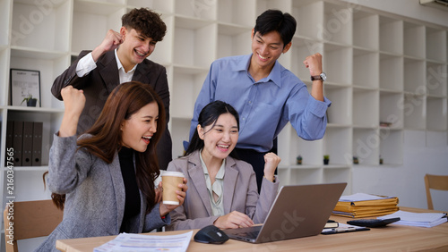 Happy diverse business team celebrating project success around a laptop.