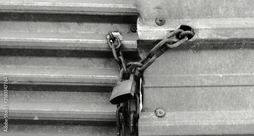 Rusty chain and padlock locking a metal roll up door, in black and white.