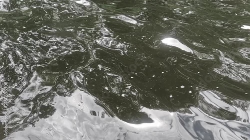 The dark green water of the lake ripples and swirls evenly, and patterns of white reflections of the sun are formed on the surface, moving in a smooth motion throughout the entire clip.