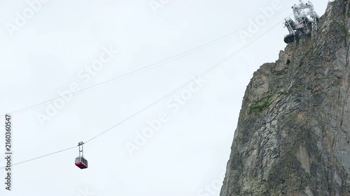 Brevent cable car red cabin ascending towards top summit station on steep rocky cliff in Chamonix Mont Blanc valley, alpine gondola ropeway transport in French Alps mountain landscape during summer