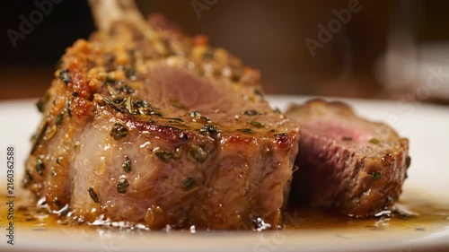 Gourmet roasted rack of lamb with herb crust and savory jus, presented on a white plate. Close-up of a perfectly cooked medium-rare lamb chop.