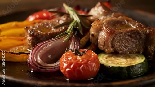 Gourmet Roasted Pork Fillet Medallions with Glaze, Rosemary, and Charred Vegetables including Yellow Peppers, Red Onions, and Cherry Tomatoes on a Dark Platter.