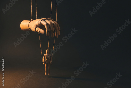 Marionette puppet under giant hand in a dark power control concept scene