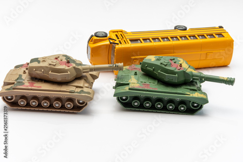Two toy tanks facing each other beside overturned yellow school bus