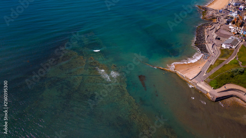 Aerial view of The Cobb and historic harbour in Lyme Regis, with the stone breakwater extending into the turquoise English Channel along the Jurassic Coast, Lyme Regis, England, United Kingdom.