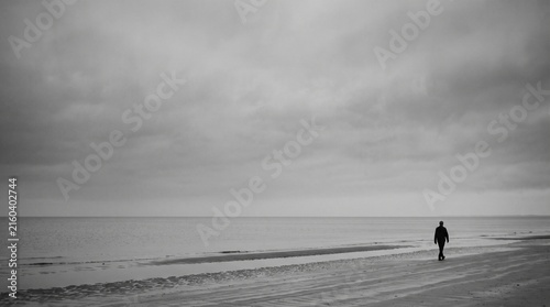 Stormy Beach Landscape with Surfer and Man Walking Along the Shore Under Dramatic Skies and Powerful Ocean Waves at Sunset