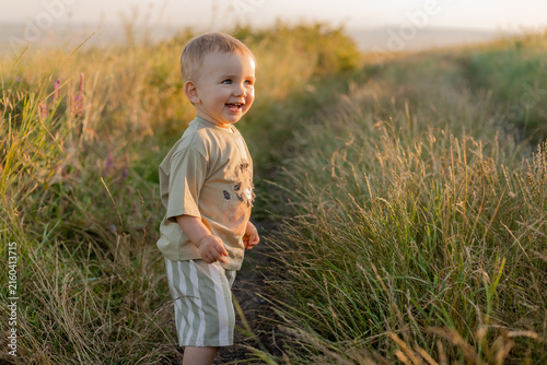 happy 2‑year‑old blond boy in the field at sunset.