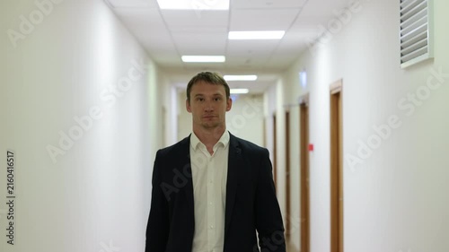 Successful male executive in a formal suit walking through a bright corporate hallway directly towards the camera.Split screen or sequence of a professional businessman walking back and forth in a con