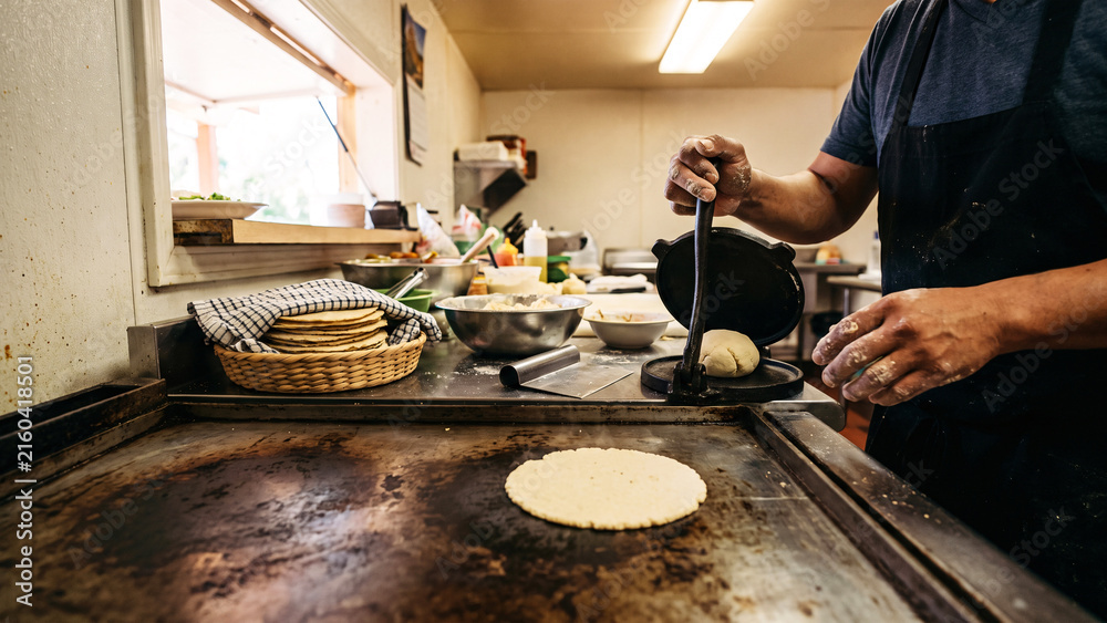 Fototapeta premium Cook Pressing Masa and Cooking Corn Tortillas on a Steel Comal in a Family Taqueria, Traditional Mexican Kitchen, Handmade Tortillas, Authentic Regional Cooking
