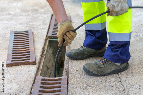 Sewer worker unclogging blocked drain grate with water jetting hose.