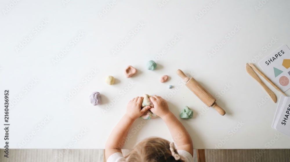 Fototapeta premium caucasian child hands playing with colorful playdough on white table. wooden rolling pin, shape cards. early childhood education, creativity, fine motor skills. copyspace, banner, website header.