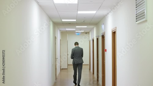 Successful male executive in a formal suit walking through a bright corporate hallway directly towards the camera.Split screen or sequence of a professional businessman walking back and forth in a con