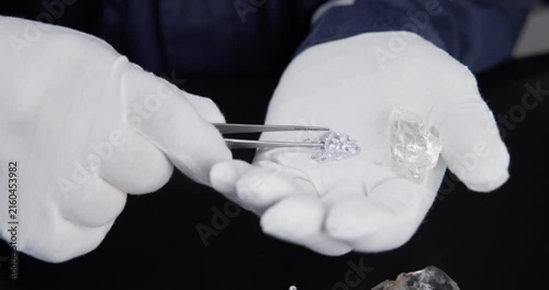 Slow motion hands placing artificial laboratory diamonds and rough crystals into gloved palm on black table.