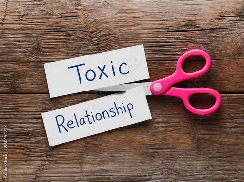 Scissors cutting toxic relationship label on paper. Emotional concept of ending harmful partnerships with symbolic separation.