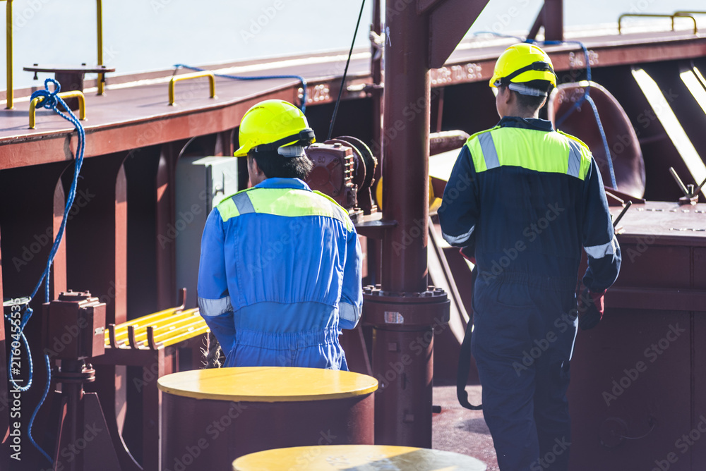Fototapeta premium Crew members preparing mooring equipment on the bow of a commercial cargo ship before entering port, handling mooring ropes, winches and heaving lines during routine deck operations.