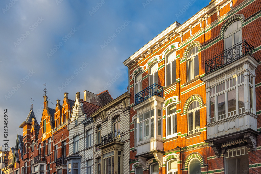Fototapeta premium Historic European Architecture Lineup with Ornate Facades and Vibrant Brickwork Under a Bright Blue Sky. Ghent town in Belgium, Europe.