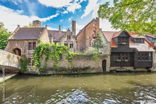 Bruges town in Belgium, Europe. Historic European architectural scenery with ancient buildings, stone bridge, and canal under a vibrant blue sky with clouds