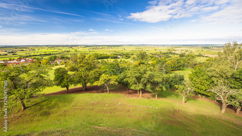 Panoramic rural landscape with rolling green hills, lush trees, distant village, and bright blue sky on a clear day. Region of Bavaria in Germany, Europe.