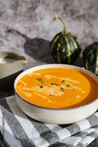 Bowl of creamy pumpkin soup topped with pumpkin seeds. Rich orange puree is served in rustic bowl and decorated with crunchy seeds creating an appetizing autumn meal presentation. Concept of seasonal