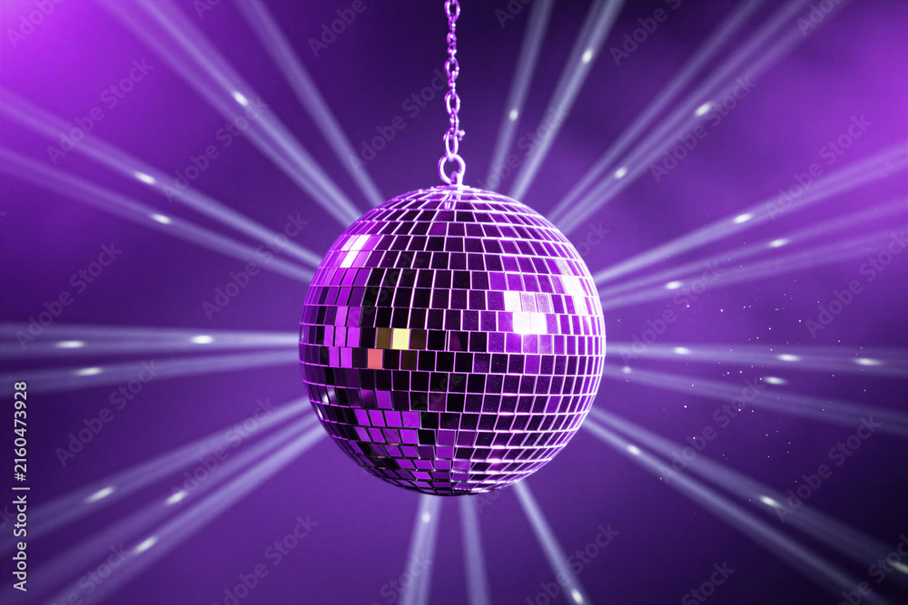 Obraz premium Shiny disco ball hangs against purple backdrop with light rays. Festive party sphere reflects lights creating dynamic motion. Celebrate with retro dance floor accessory.
