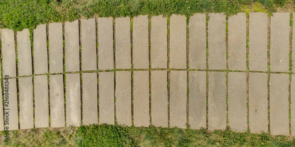 Fototapeta premium top view of the texture of paving slabs on pedestrian path with grass