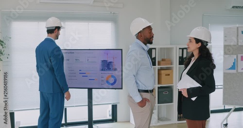 Portrait of multiracial construction engineers team discusses project in company office. Colleagues talk as manager studies construction plans in boardroom