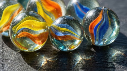 Colorful glass marbles with swirls on dark stone surface in bright sunlight