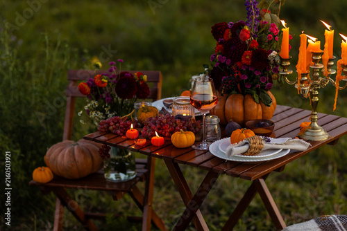 Cozy autumn table decoration for a thanksgiving party outdoors. Grapes, fig, rose wine, candles, pumpkins as decor. Elegant wedding fall arrangement, beautiful setting for a romantic proposal