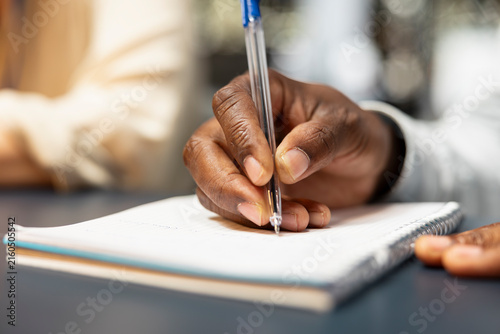 Canvas Print Bookkeeper in the office writes financial figures on paper, transcribing information with a pen and crosschecking data from reports and a notepad during late-night accounting work