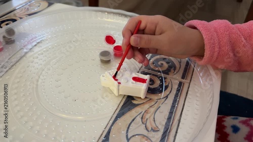 Child painting small craft figure with brush, creative activity close up