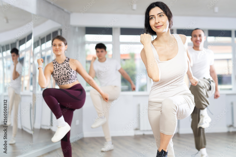 Fototapeta premium Sporty smiling young brunette practicing rhythmic aerobics during group workout in fitness studio. Active lifestyle concept