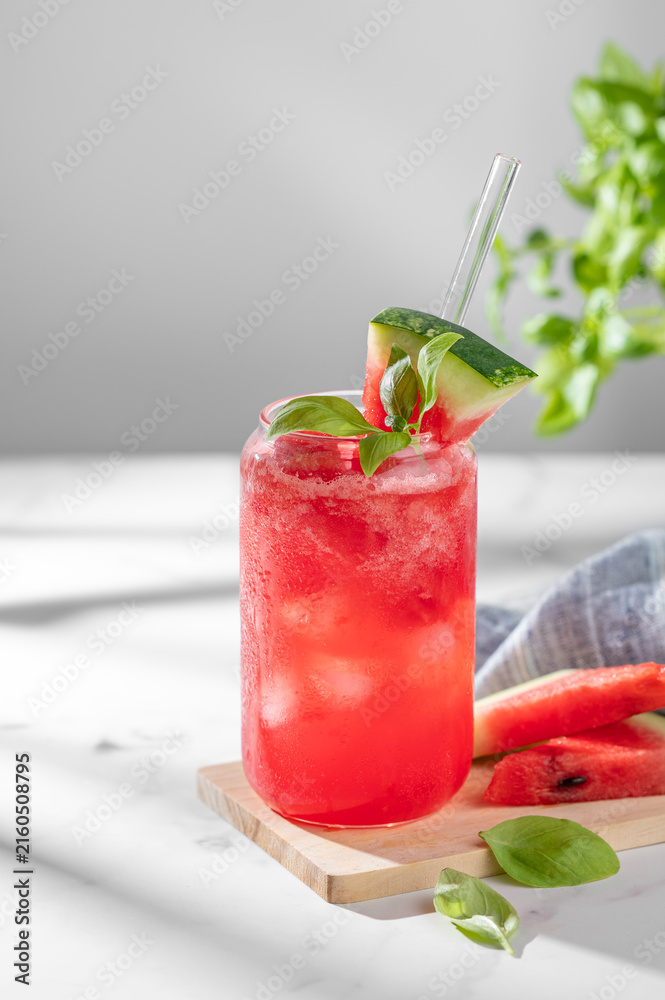 Naklejka premium A watermelon lemonade or mojito with ice and basil in a glass on a marble background
