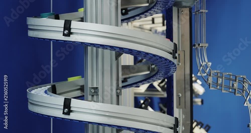 Spiral conveyor rotates within vertical automated transporting system. Curved mechanism guides continuous factory flow between production levels on plant