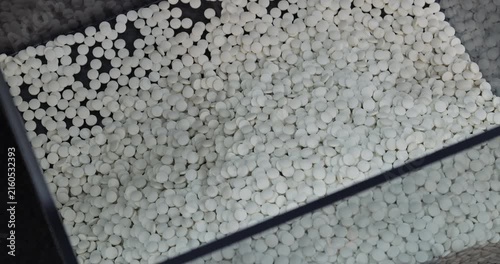 White tablets fall into collection hopper joining processed medicine batch. Automated feeder transfers fresh units from upper pharmaceutical production stage