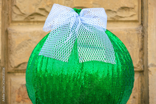 Fotografie Sparkling green decorative ball with white bow against stone wall