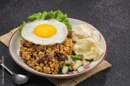 A plate of fried rice with lamb, fried egg, tomato, shrimp crackers, cucumber and lettuce isolated on wooden textured. Nasi Goreng Kambing, indonesian food