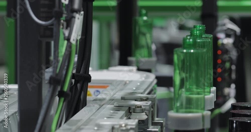 Automated production line transports green plastic bottles through modern manufacturing facility. Precision equipment ensures efficient packaging operations